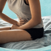 Femme assise sur un lit tenant son bas-ventre avec une zone rouge illustrant une douleur pelvienne liée aux règles douloureuses.